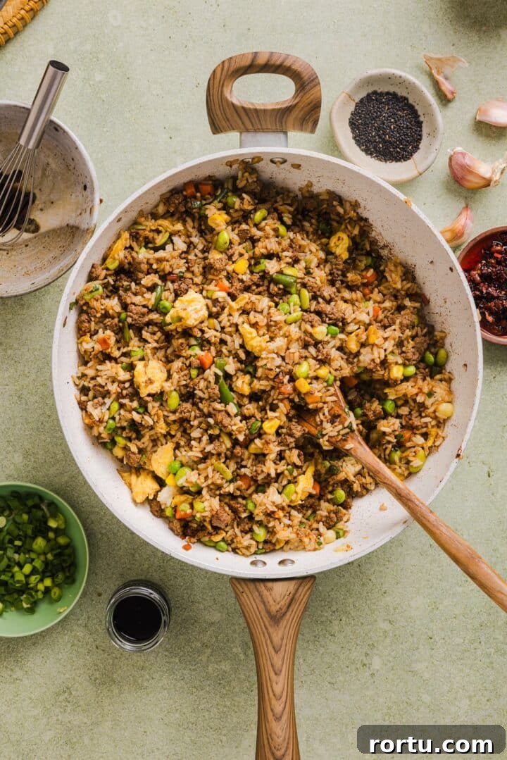 Savory Ground Beef Fried Rice Recipe for Weeknight Dinners 7 Beef fried rice in a large pan with a wooden spoon.