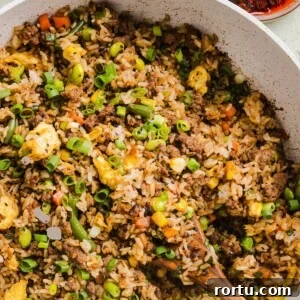 Ground beef fried rice in a large saute pan with a wooden spoon.