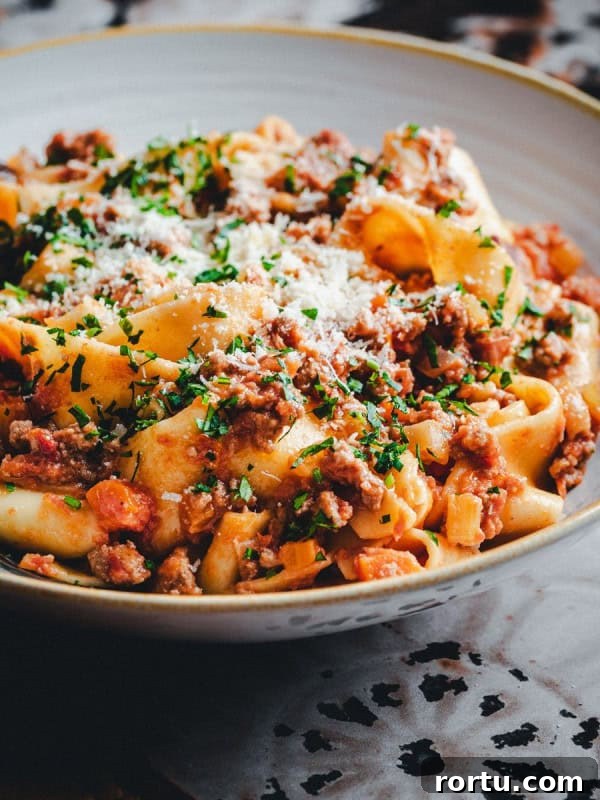 Lamb Ragu Recipe: Slow-Simmered Sauce with Parmesan 14 Close-up of a bowl of pasta topped with ground lamb sauce, garnished with grated cheese and chopped herbs.