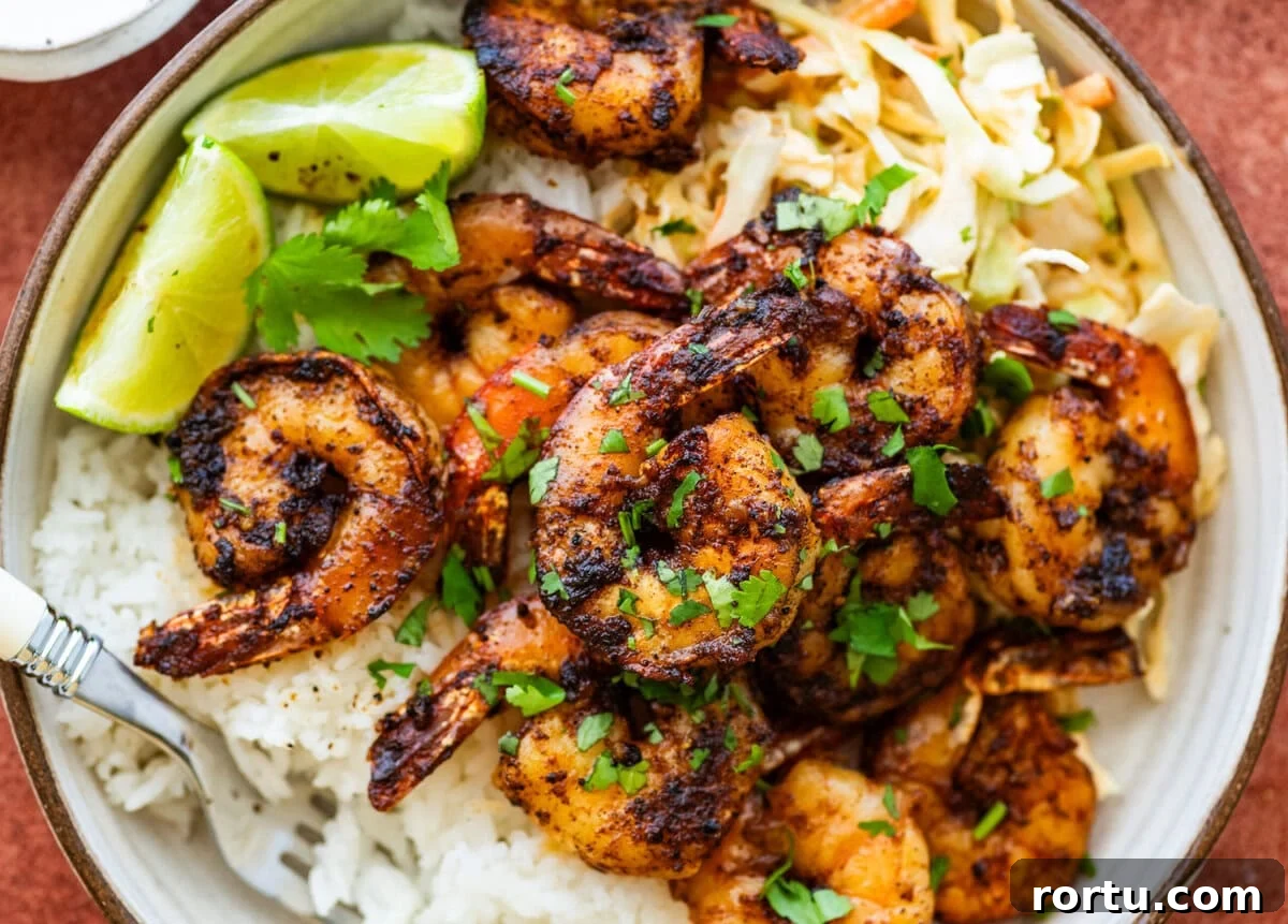 10-Minute Blackened Shrimp Recipe for Flavorful Weeknight Meals 2 Blackened shrimp on a plate that contains rice and garnish.