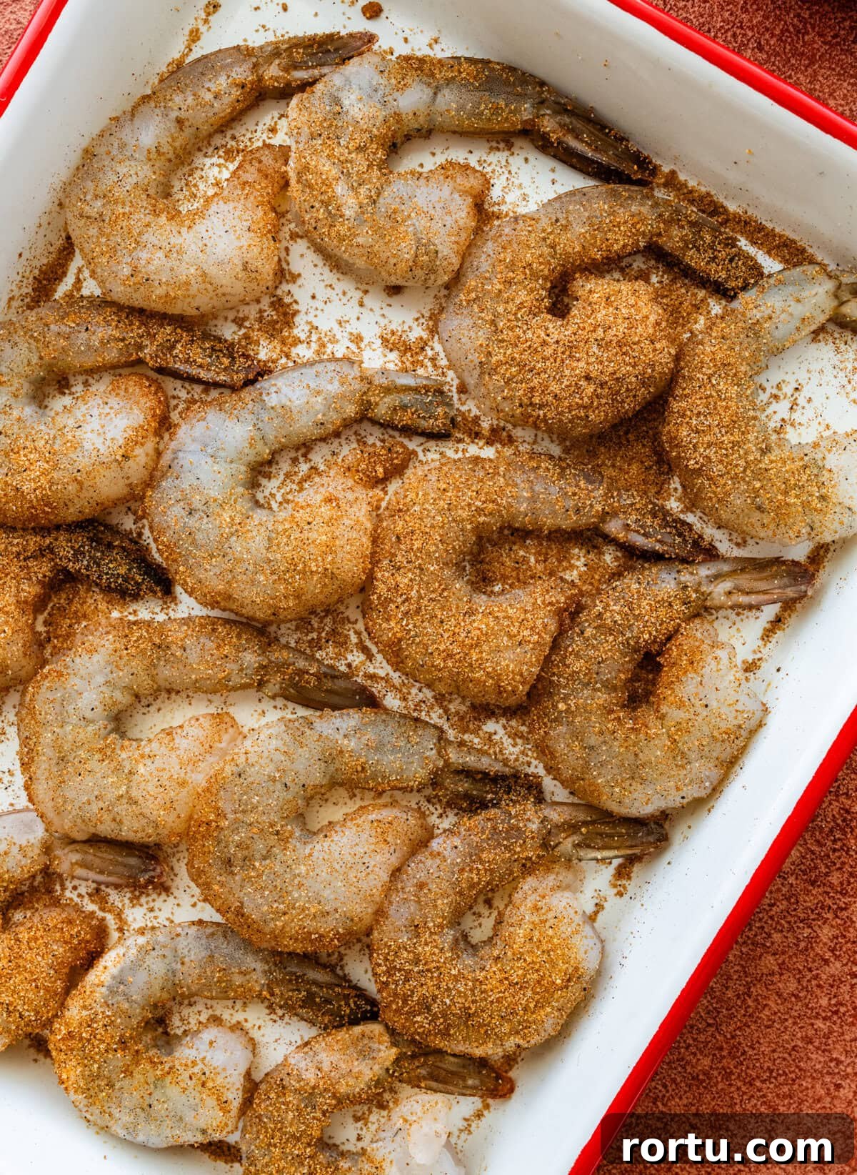 10-Minute Blackened Shrimp Recipe for Flavorful Weeknight Meals 8 Raw shrimp in a dish covered with blackened seasoning.
