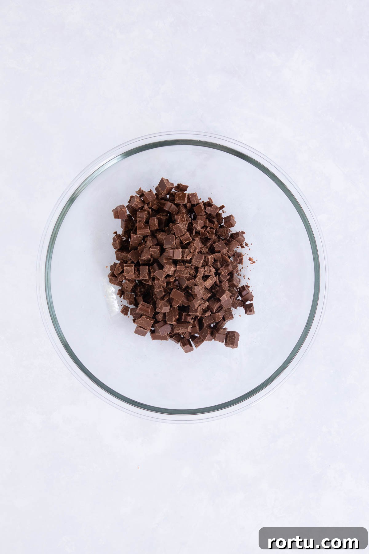 Creamy Baileys Chocolate Mousse Recipe 4 Chopped milk chocolate in a large glass mixing bowl, on a grey marble background.