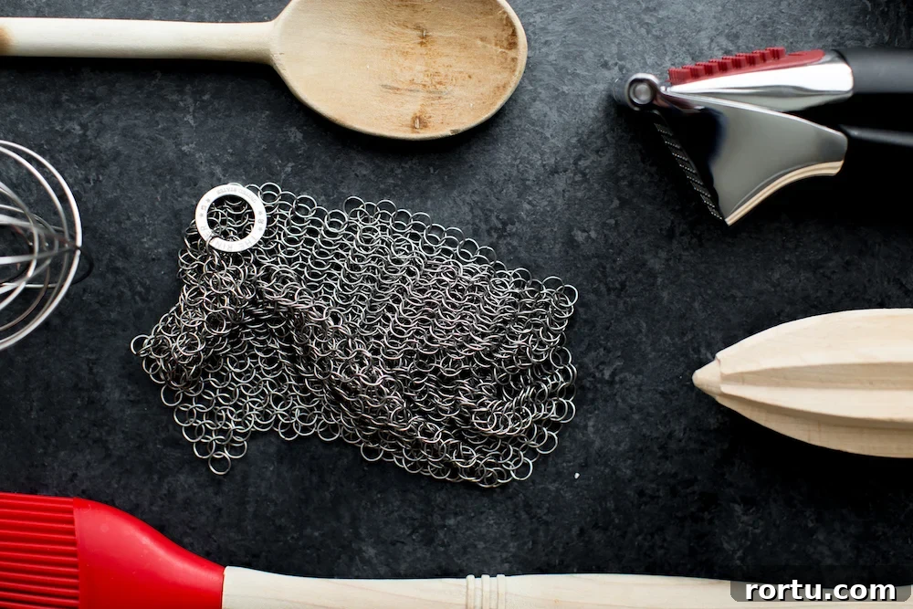 kitchen equipment including garlic press citrus reamer wooden spoon and chain link scrubber on dark background