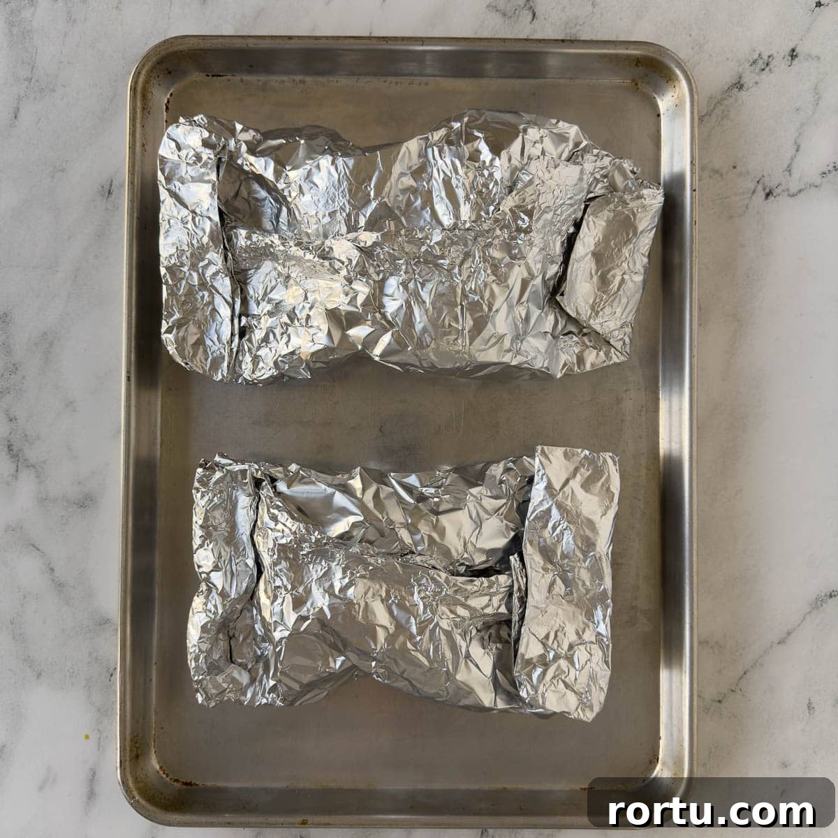 Aluminum foil packets on a rimmed baking sheet.