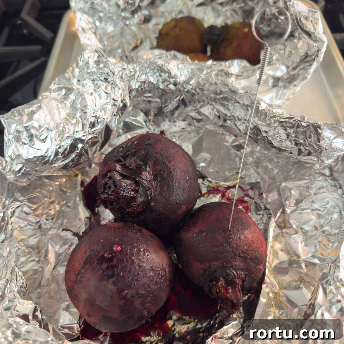 Roasted beets in foil with a skewer piercing one to show doneness.