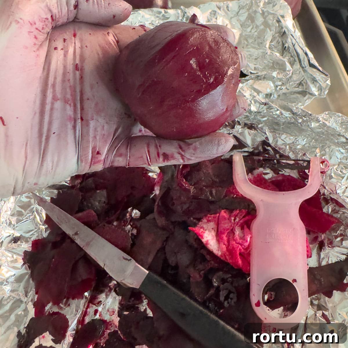 A gloved hand holding a peeled red beet with peeler and knife.
