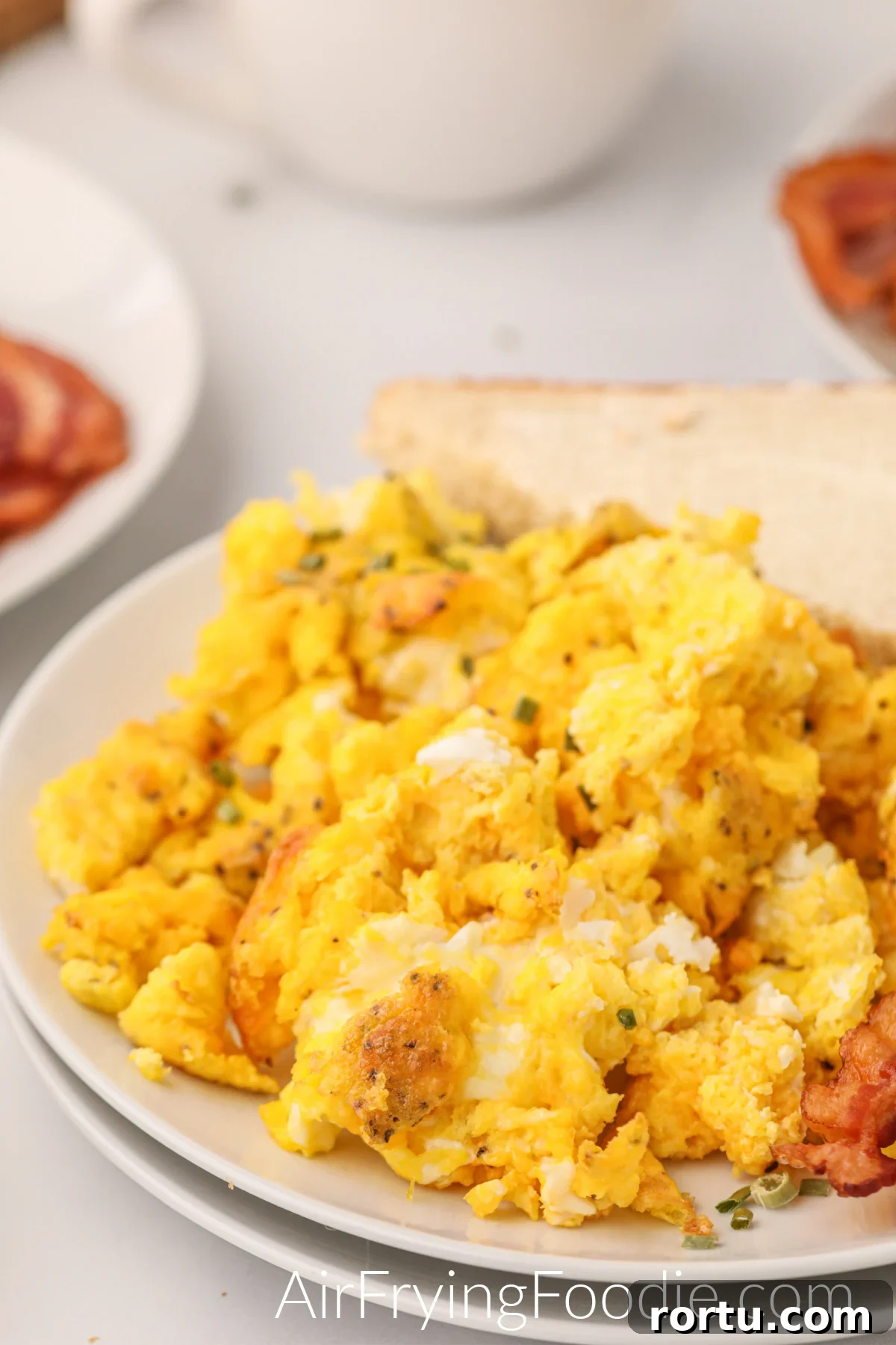 Air fryer scrambled eggs on a plate with bacon and toast.