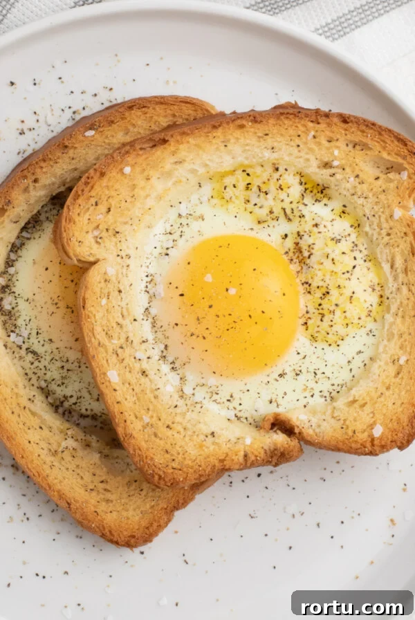 Eggs in a basket made in the Air Fryer and served on a white plate, sprinkled with salt and pepper.