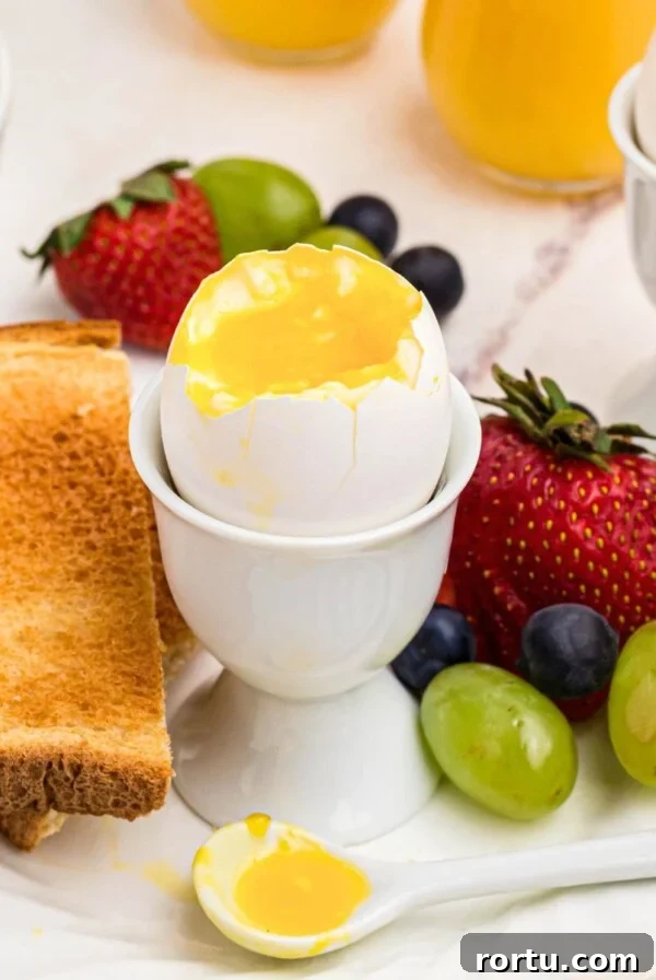 Slightly runny yolk inside of an egg shell in an egg holder with fruit and toast.