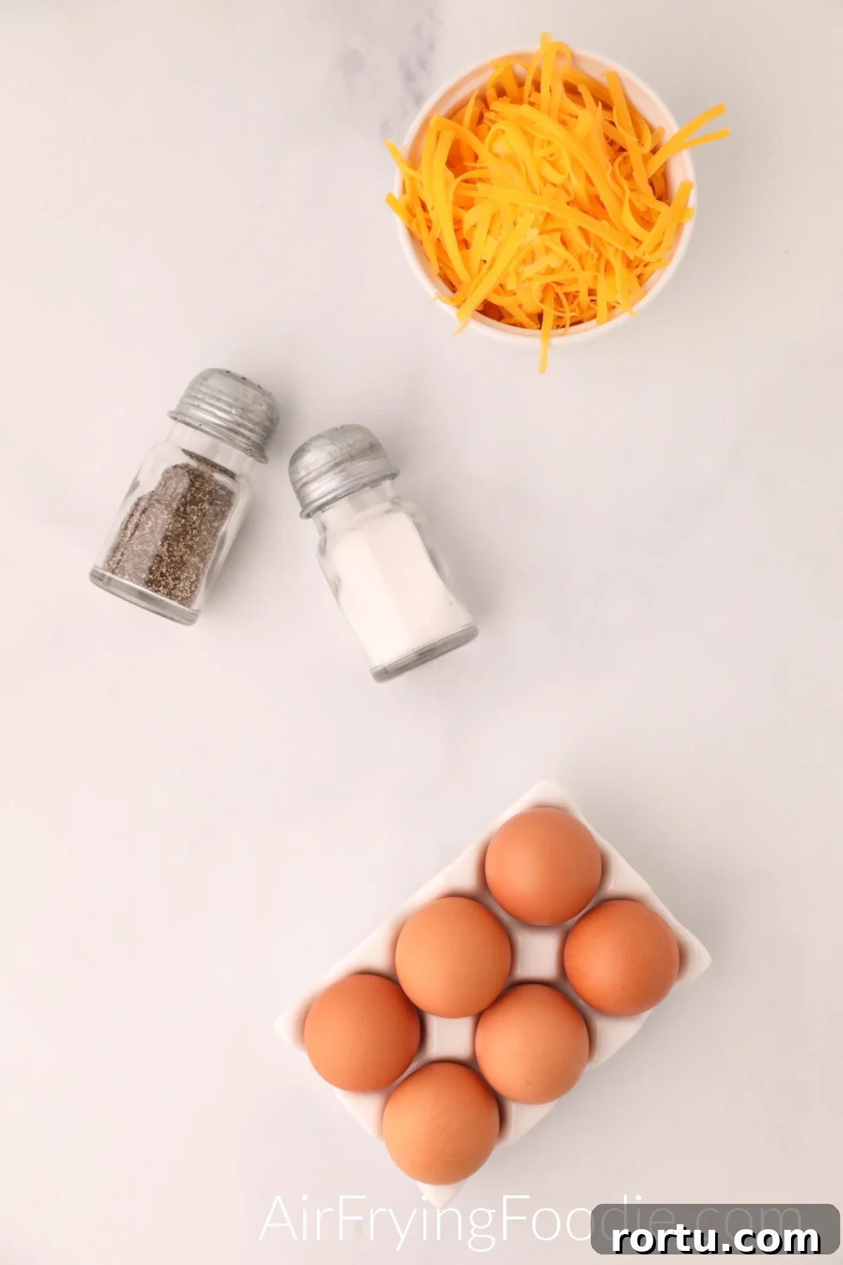 Ingredients needed to make scrambled eggs in the air fryer - cheese in a bowl, salt and pepper, and eggs.