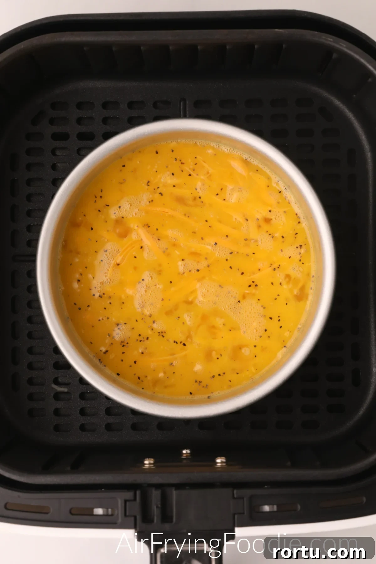 Whisked eggs and cheese in a bowl in the basket of the air fryer.
