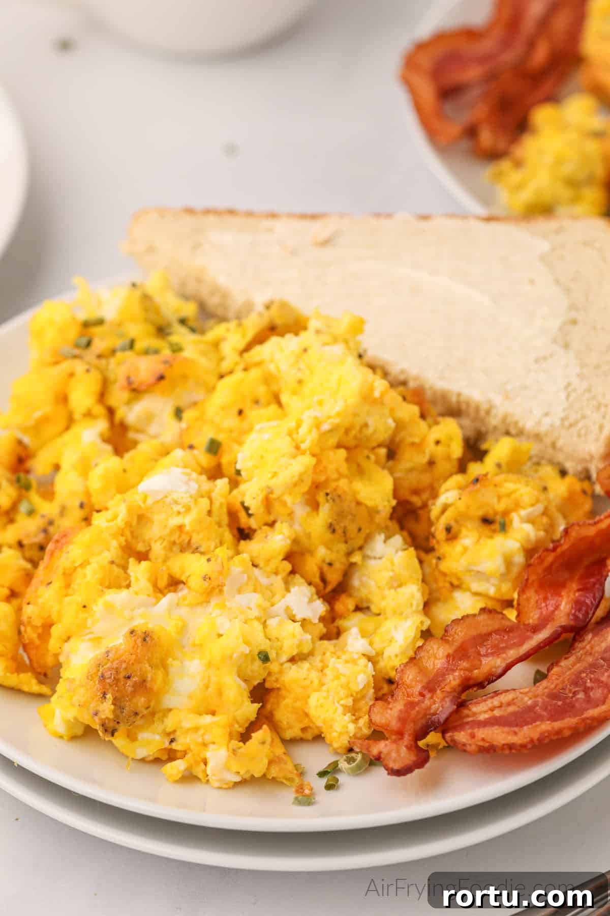 Fluffy air fryer scrambled eggs on a plate with bacon and a side of buttered bread.