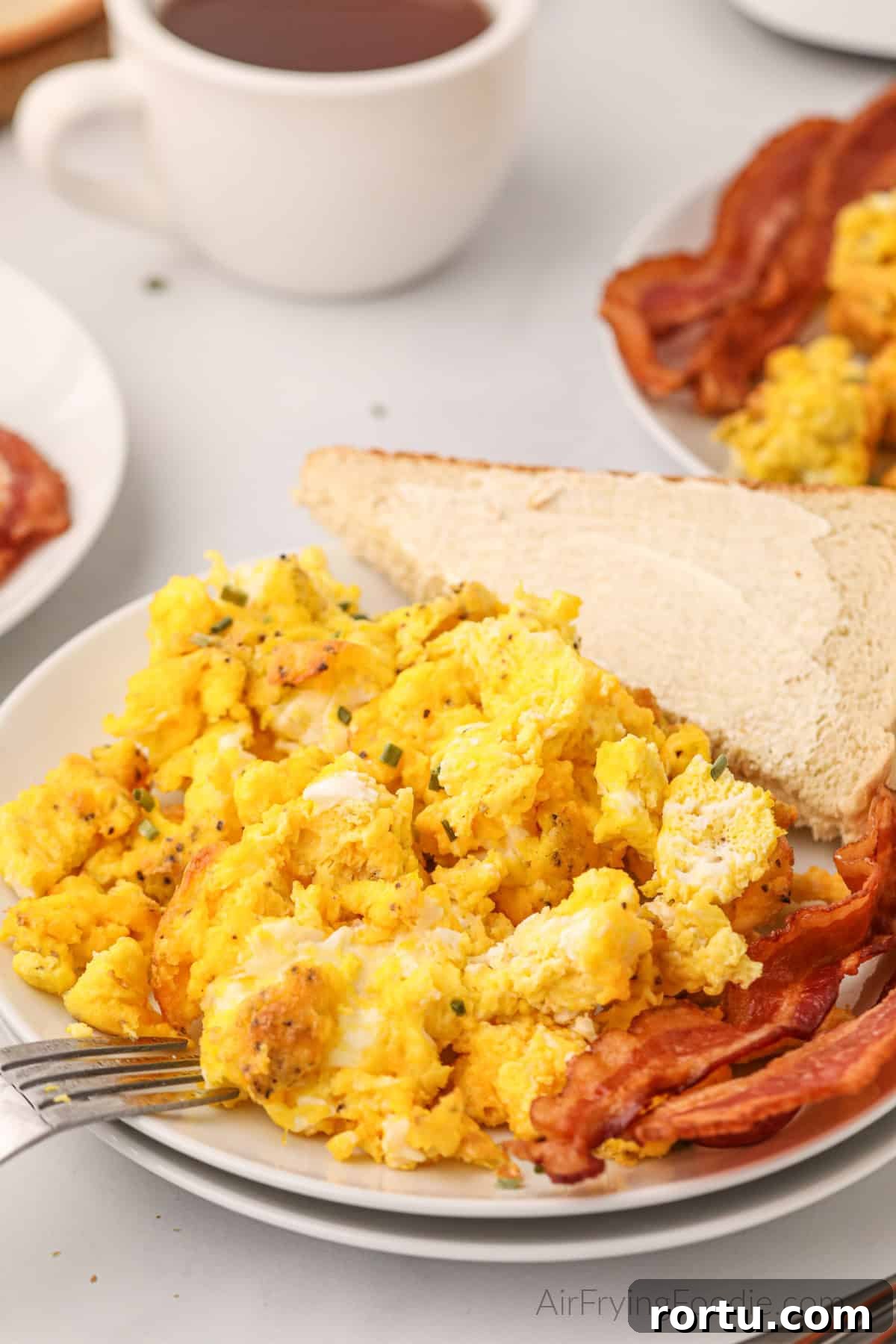 Air fried scrambled eggs on a plate with bacon and a side of buttered bread.