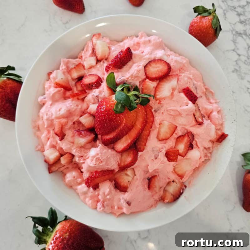 Strawberry fluff salad in a white bowl with cut strawberries for garnish