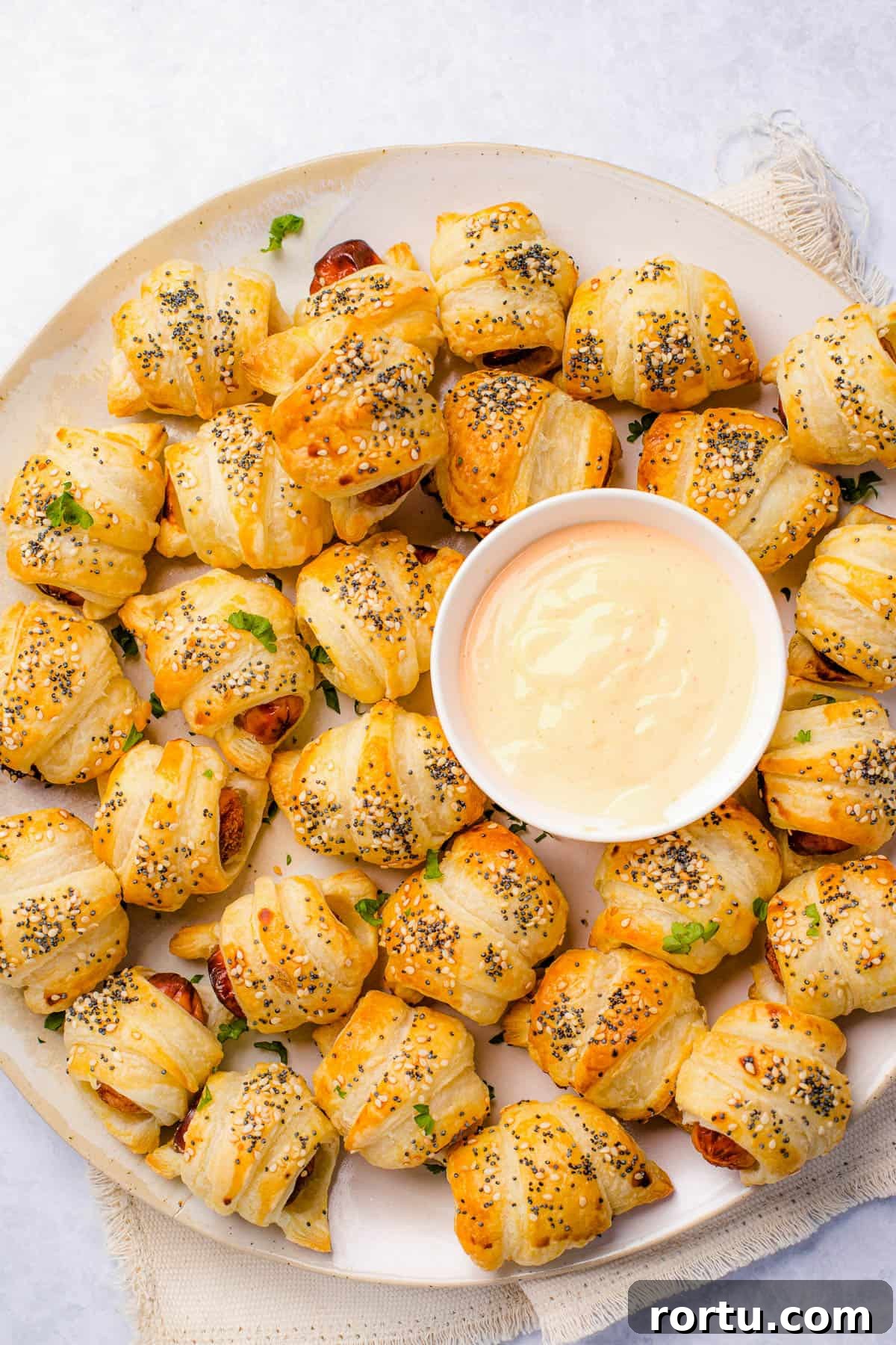 A platter of pigs in a blanket with a bowl of dipping sauce in the center.