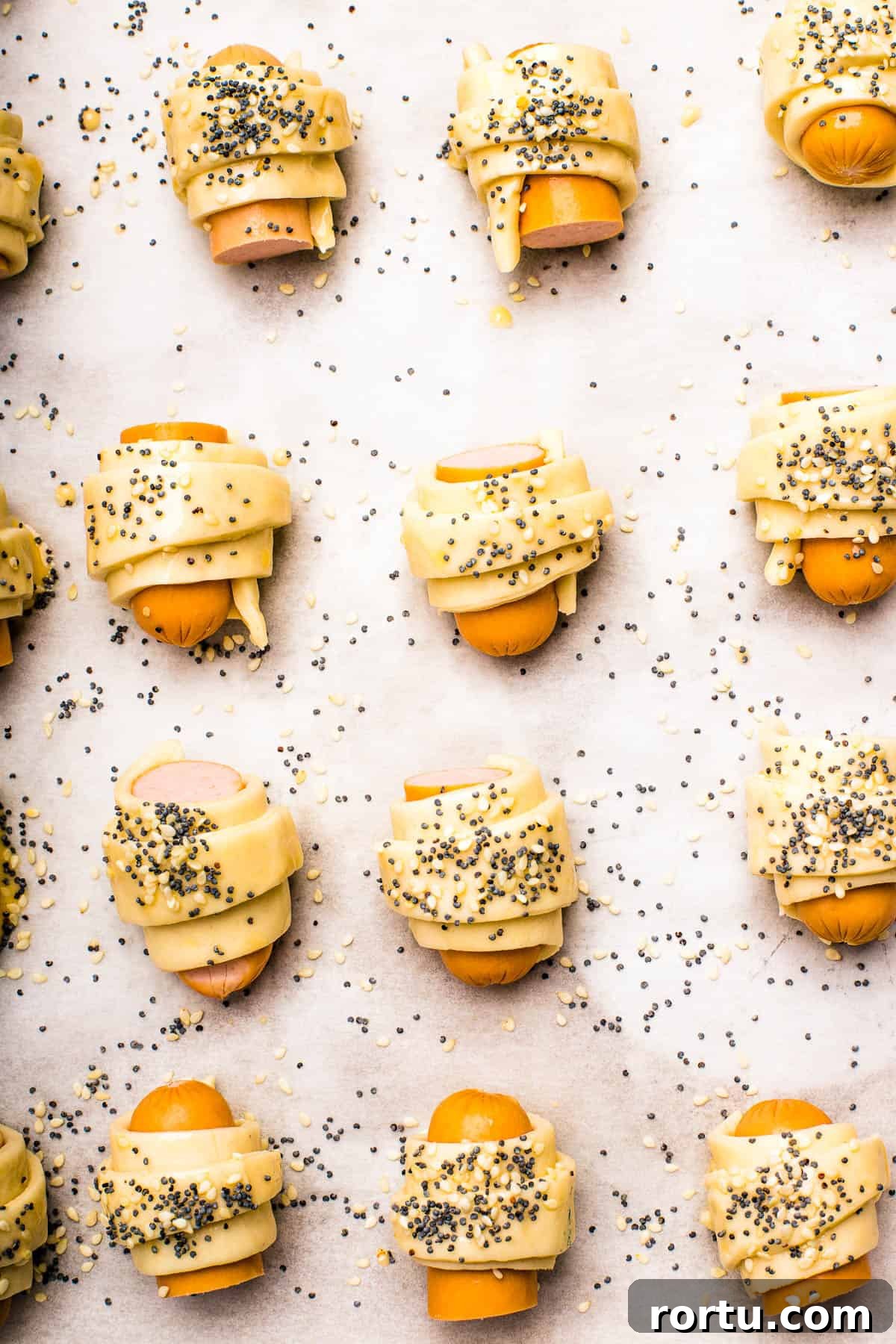 Unbaked pastries brushed with egg wash and sprinkled with sesame seeds and poppy seeds.