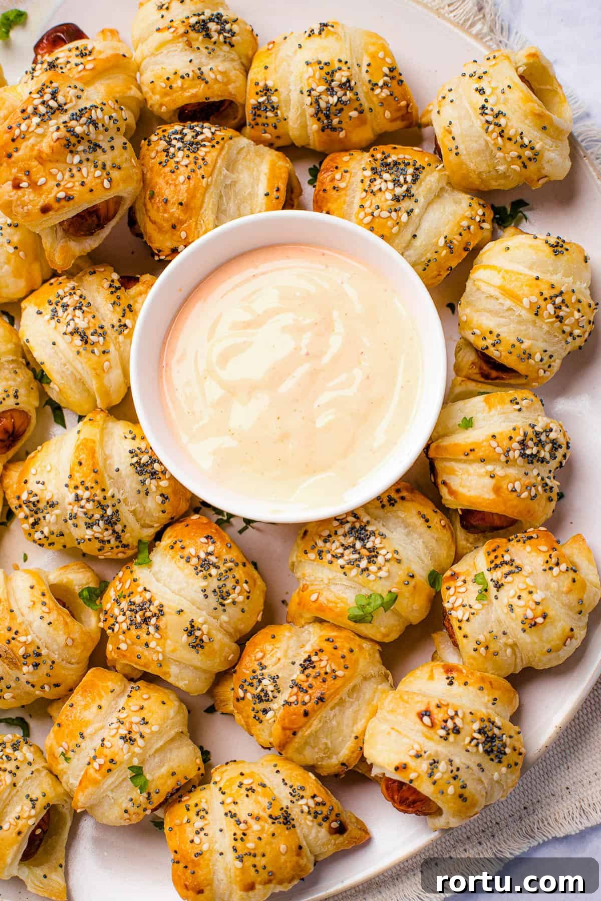 A platter of pigs in a blanket with a bowl of dipping sauce in the center.
