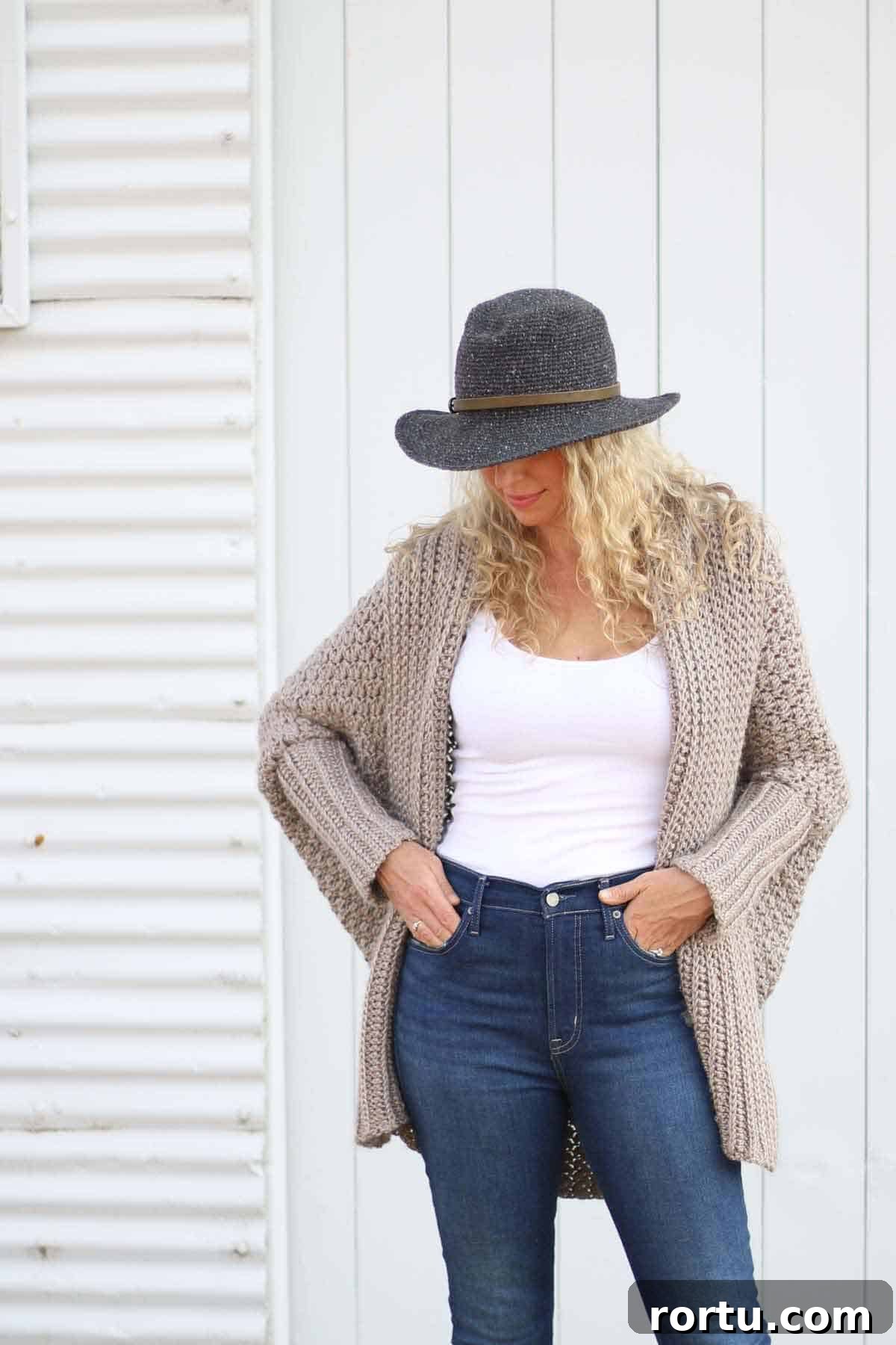 Woman wearing a rectangle crochet cardigan and a hat while looking down to the floor is shown. -Skip To My Lou