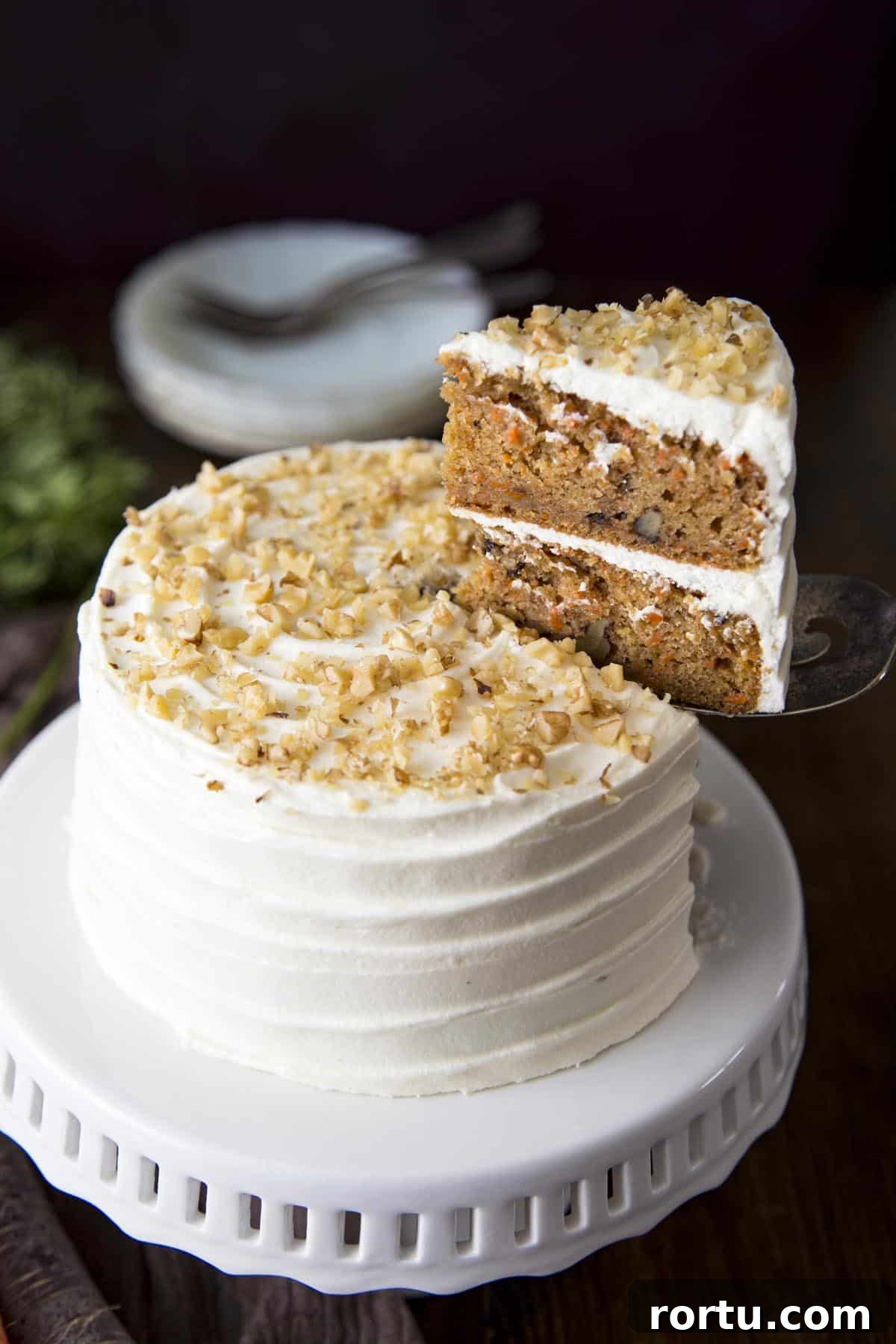 A mini carrot cake on a white cake stand with a slice being cut.