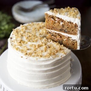 A mini carrot cake on a white cake stand with a slice being cut.